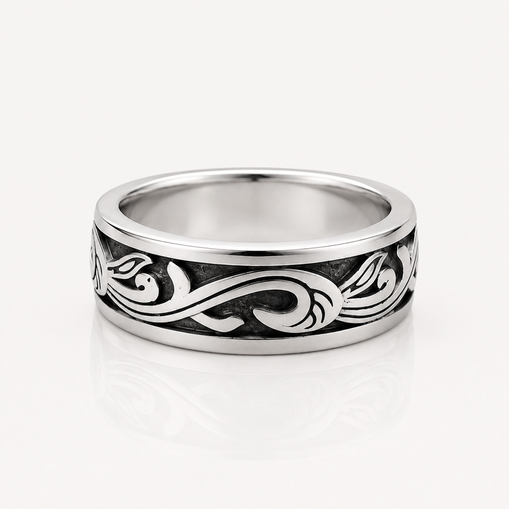 A silver band ring with a polished finish and an engraved black scrollwork pattern, shown on a clean white background with a soft reflection.