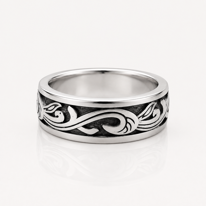 A silver band ring with a polished finish and an engraved black scrollwork pattern, shown on a clean white background with a soft reflection.