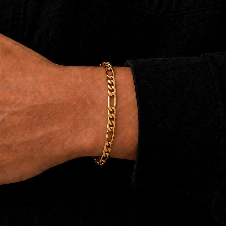 A close-up of a person's wrist wearing a gold chain bracelet against a black shirt background.