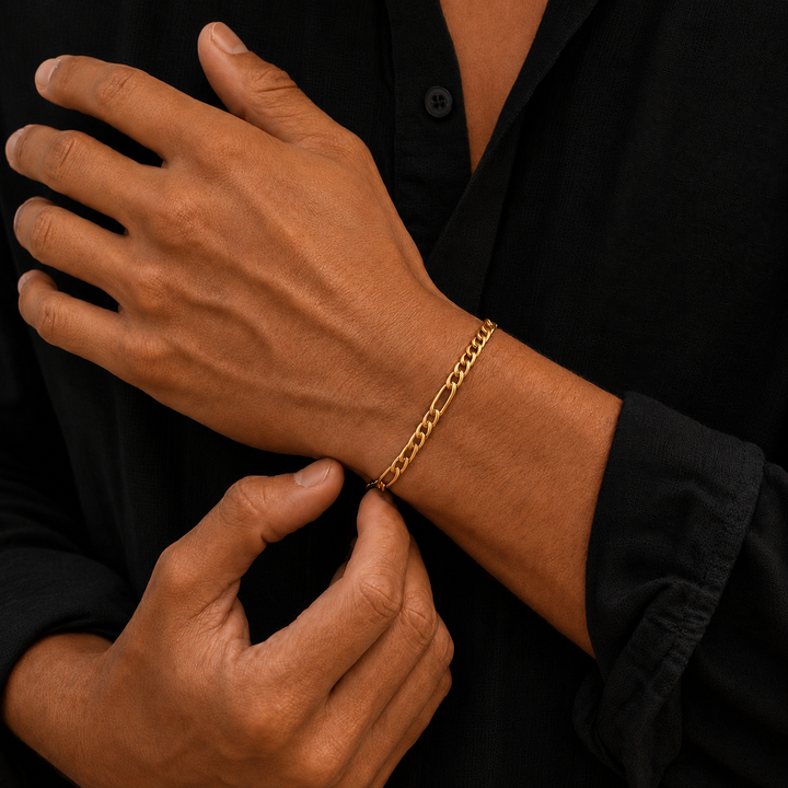 A close-up of a man's wrist wearing a gold chain link bracelet, with his other hand resting on his chest. He is wearing a black button-down shirt.