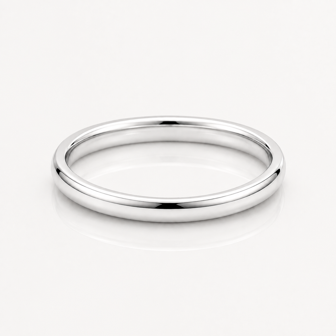 A minimalist, polished silver band ring with a smooth, rounded profile, displayed on a clean white reflective surface.