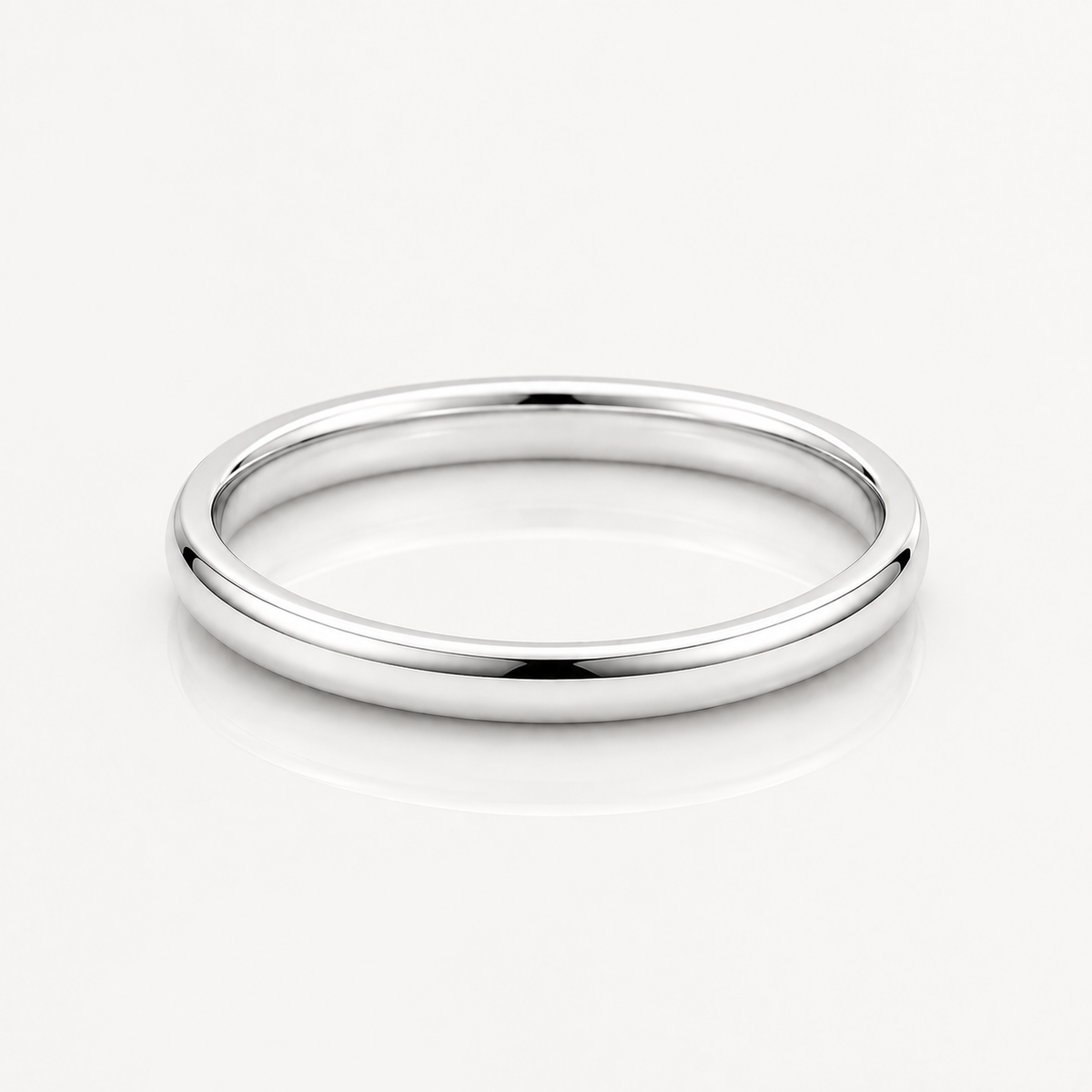 A minimalist, polished silver band ring with a smooth, rounded profile, displayed on a clean white reflective surface.