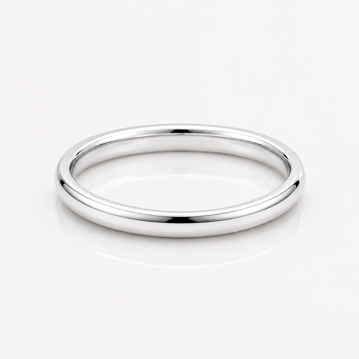 A minimalist, polished silver band ring with a smooth, rounded profile, displayed on a clean white reflective surface.