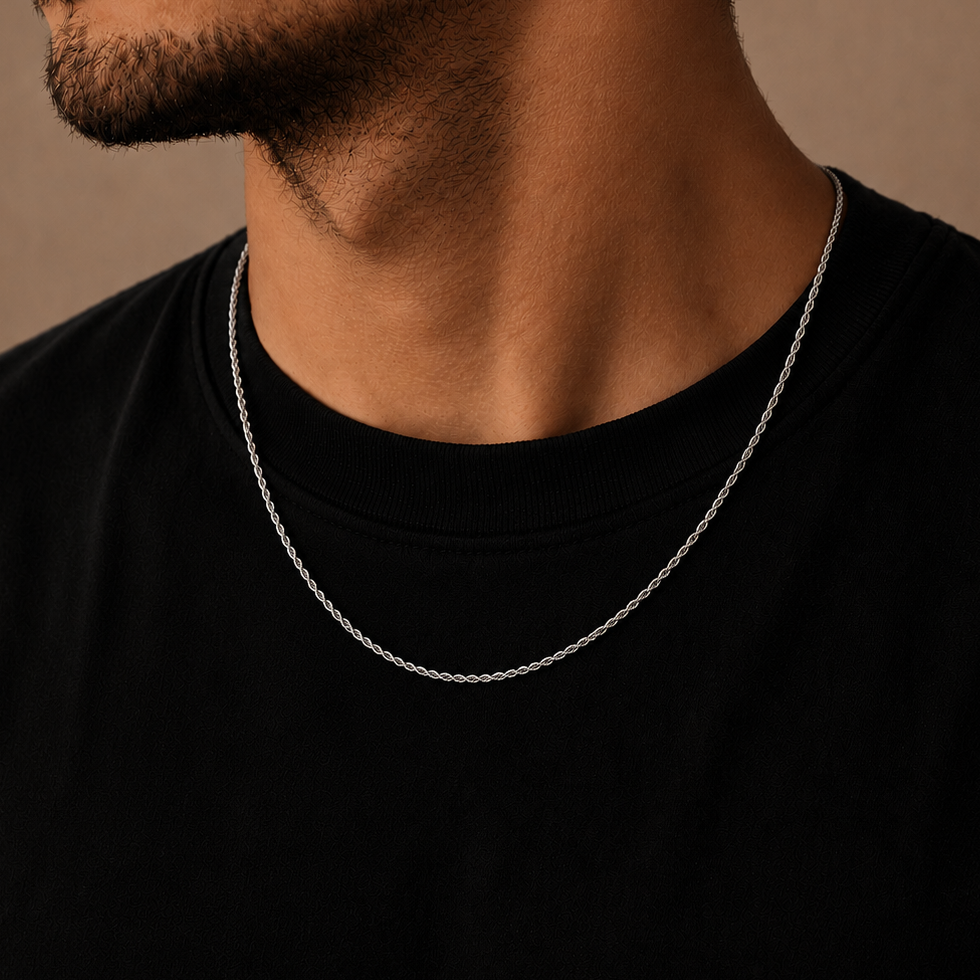 A close-up of a man's neck and lower face wearing a delicate silver chain necklace over a black t-shirt, set against a warm brown background.