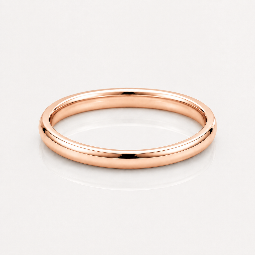 A minimalist rose gold band ring with a smooth, polished finish, shown on a clean white reflective surface.