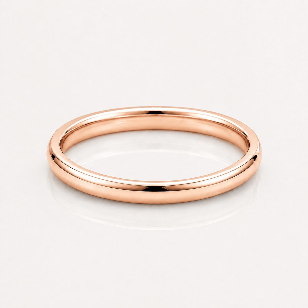 A minimalist rose gold band ring with a smooth, polished finish, shown on a clean white reflective surface.