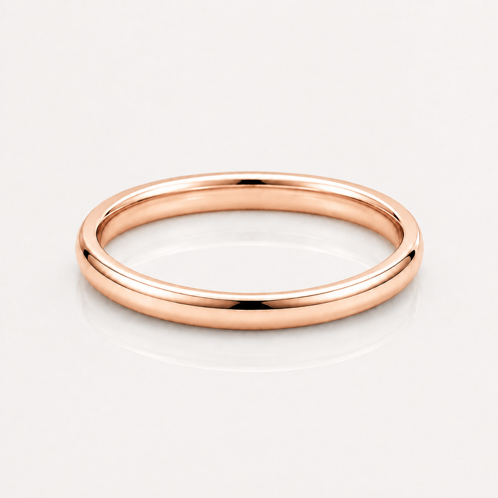 A minimalist rose gold band ring with a smooth, polished finish, shown on a clean white reflective surface.