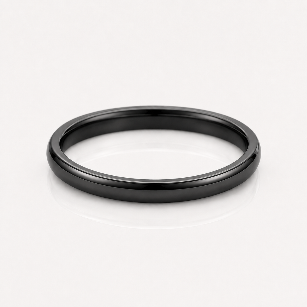 A minimalist matte black metal band ring, photographed from a top-down perspective on a clean white reflective surface.