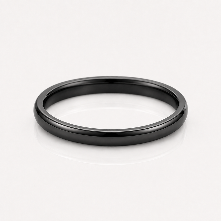 A minimalist matte black metal band ring, photographed from a top-down perspective on a clean white reflective surface.