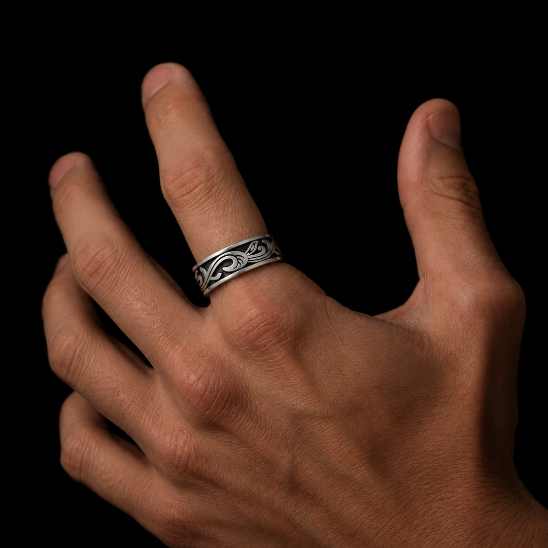 A close-up of a hand wearing a silver ring with an engraved Celtic knot pattern, set against a solid black background.