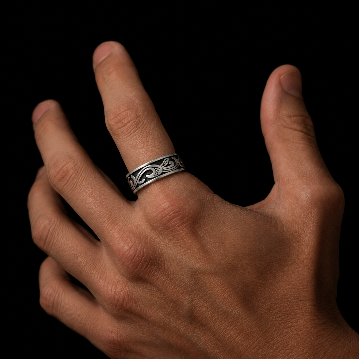 A close-up of a hand wearing a silver ring with an engraved Celtic knot pattern, set against a solid black background.