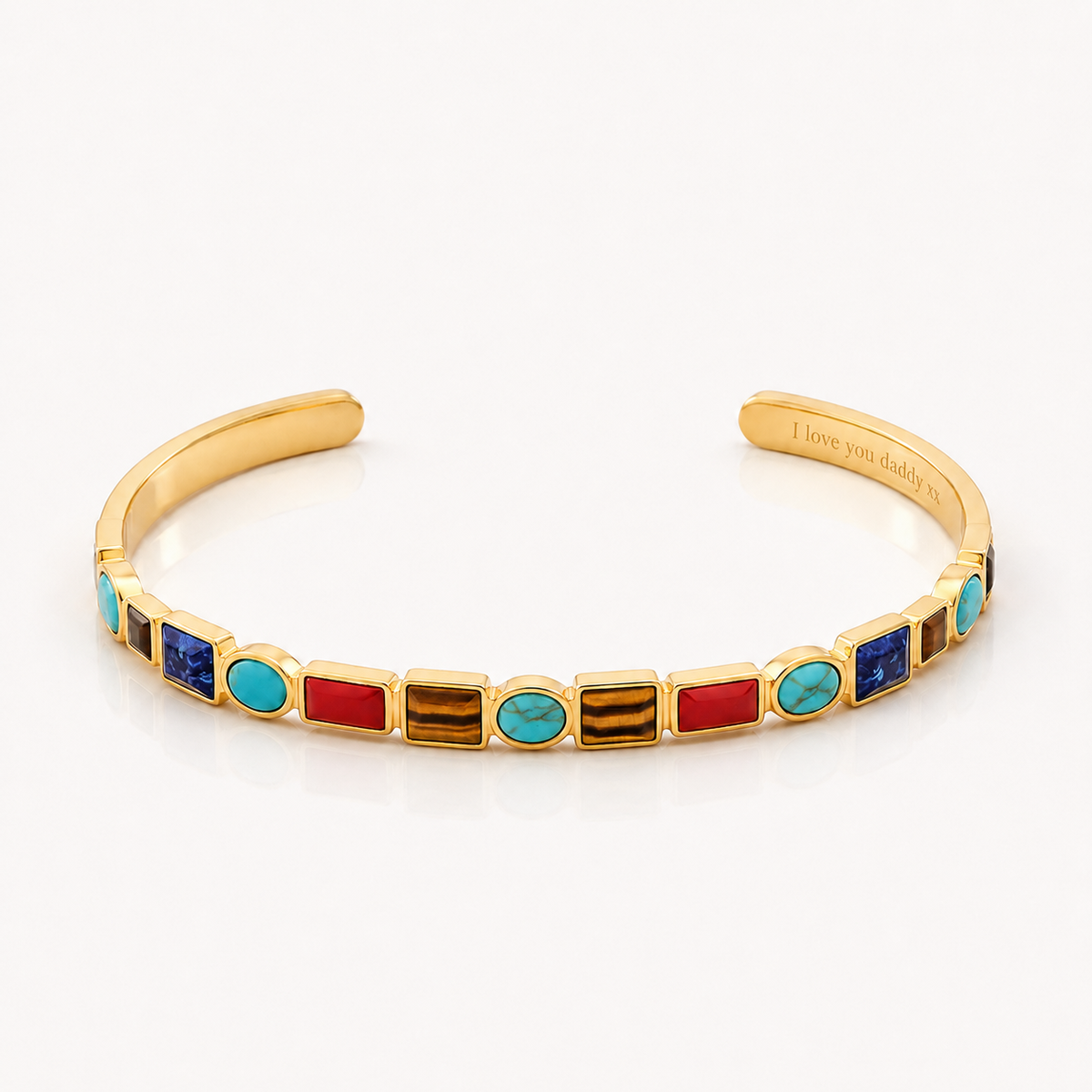A gold cuff bracelet featuring a row of colorful rectangular and oval bezel-set stones in red, turquoise, blue, and brown, displayed on a clean white background.