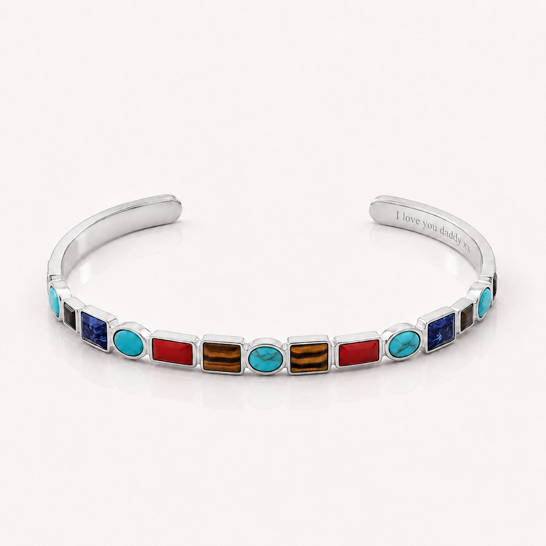 A silver cuff bracelet featuring a row of colorful inlay stones, including turquoise, red, blue, and brown, with the inner band engraved with 'I love you daddy'.