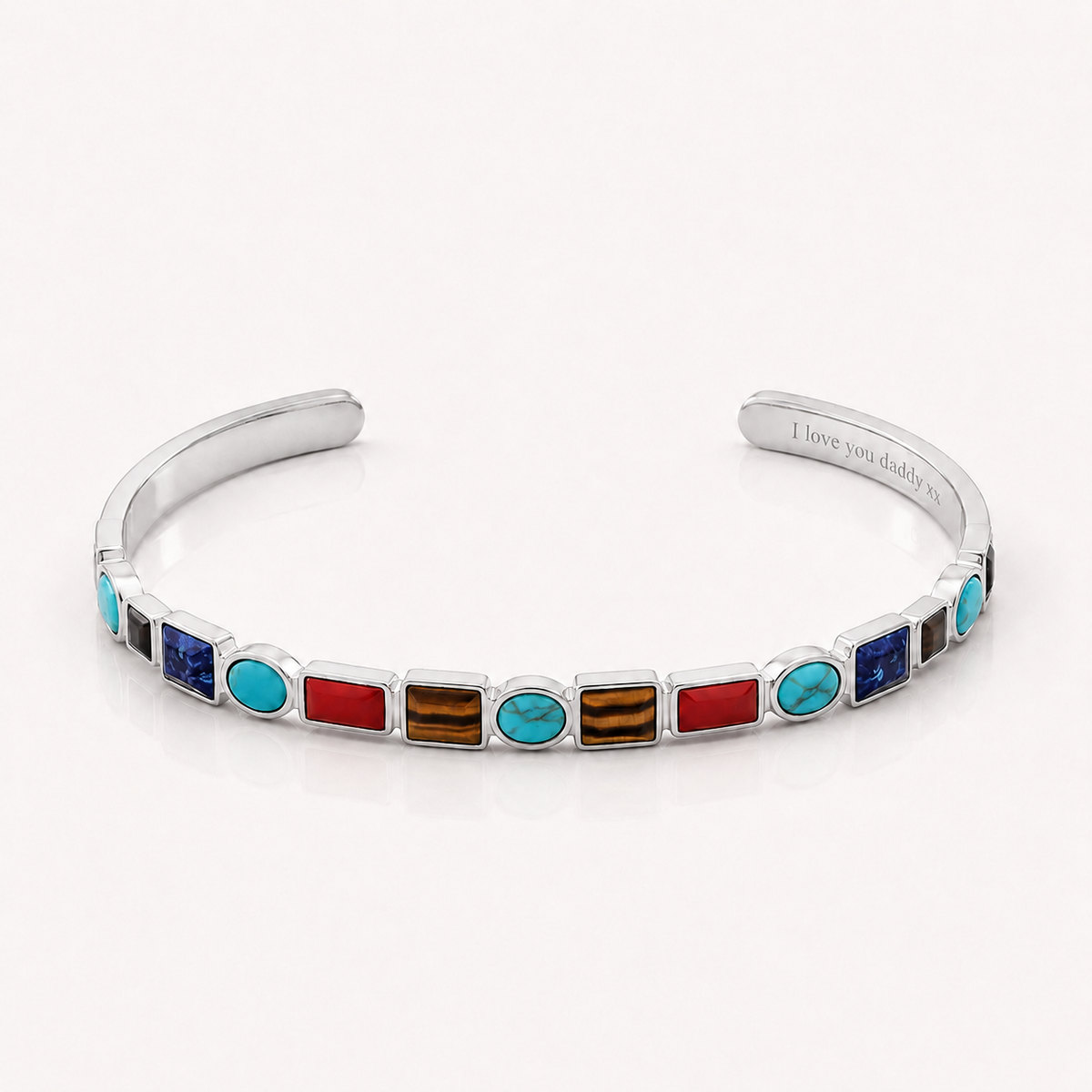 A silver cuff bracelet featuring a row of colorful inlay stones, including turquoise, red, blue, and brown, with the inner band engraved with 'I love you daddy'.