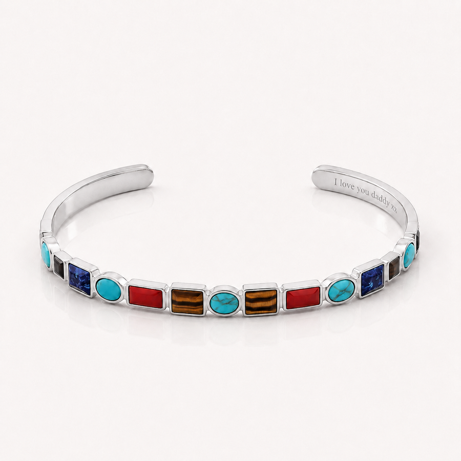 A silver cuff bracelet featuring a row of colorful inlay stones, including turquoise, red, blue, and brown, with the inner band engraved with 'I love you daddy'.