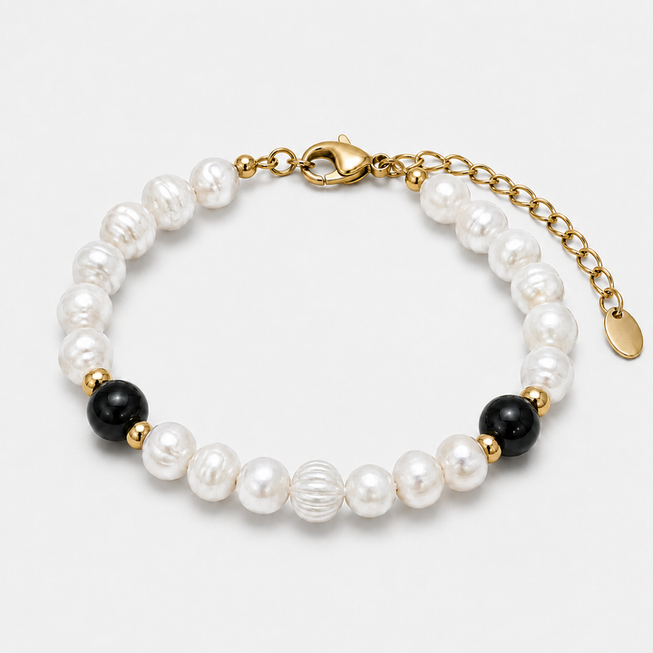 A beaded bracelet featuring white baroque pearls, two black beads, and gold spacer beads, finished with a gold lobster clasp and extender chain.
