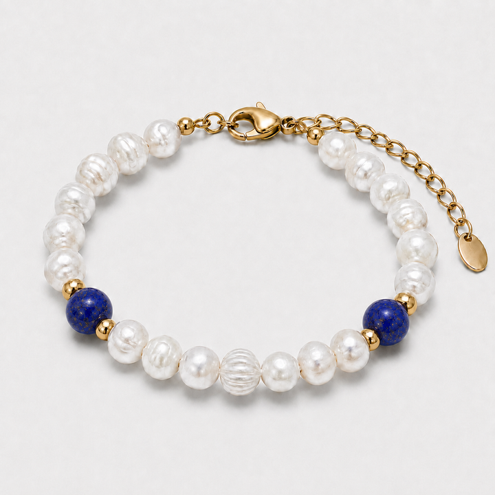A beaded bracelet featuring white baroque pearls, two deep blue lapis lazuli stones, and gold spacer beads, finished with a gold lobster clasp and extension chain.
