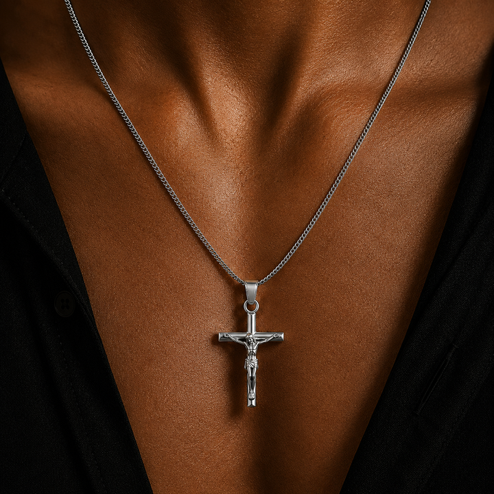 A silver crucifix pendant necklace worn on a person's chest, shown in a close-up shot with a black shirt visible.