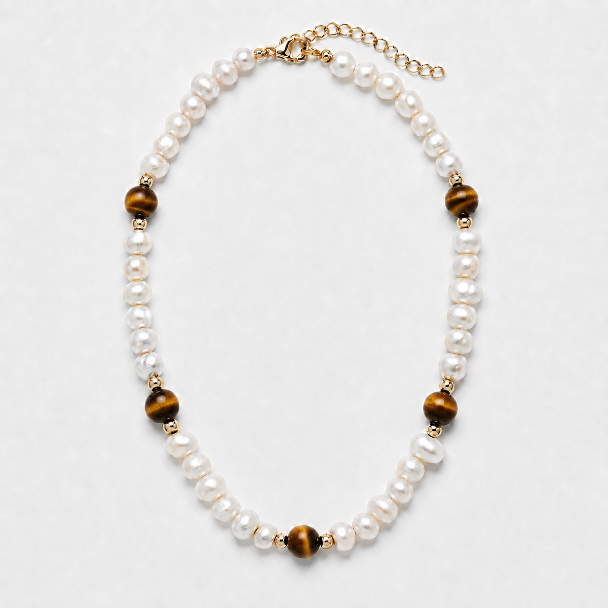 A pearl and tiger's eye bead necklace with gold-toned metal accents, displayed on a light gray background.