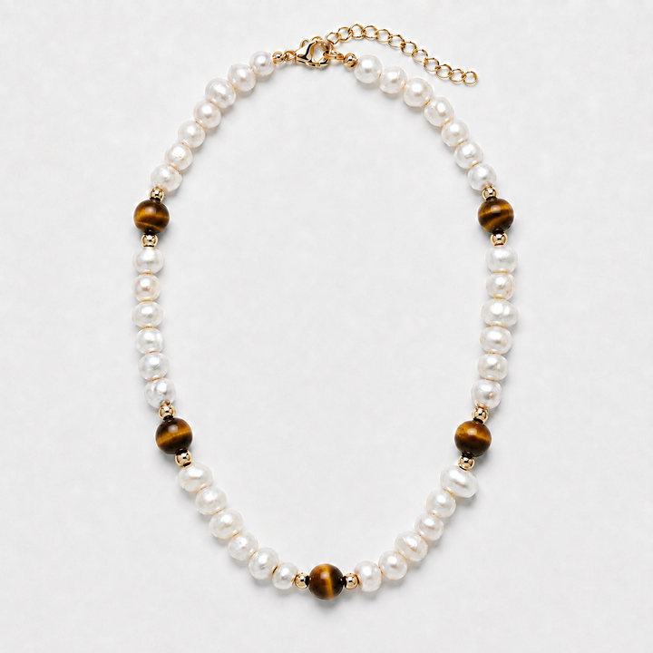 A pearl and tiger's eye bead necklace with gold-toned metal accents, displayed on a light gray background.