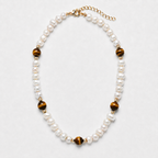 A pearl and tiger's eye bead necklace with gold-toned metal accents, displayed on a light gray background.