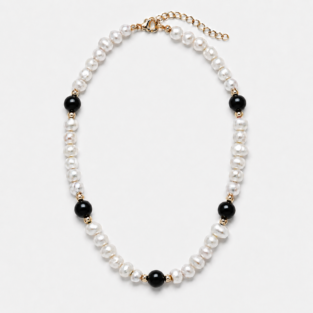 A pearl and black bead necklace with gold-tone metal accents, displayed on a clean white background.