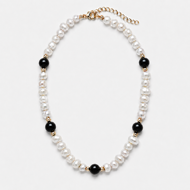 A pearl and black bead necklace with gold-tone metal accents, displayed on a clean white background.