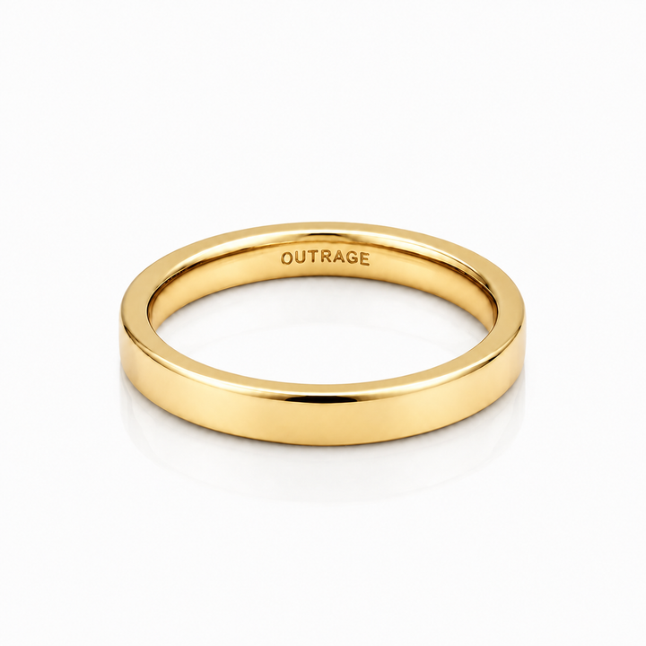 A polished yellow gold band ring with the word 'OUTRAGE' engraved inside, shown on a clean white background with a soft reflection.