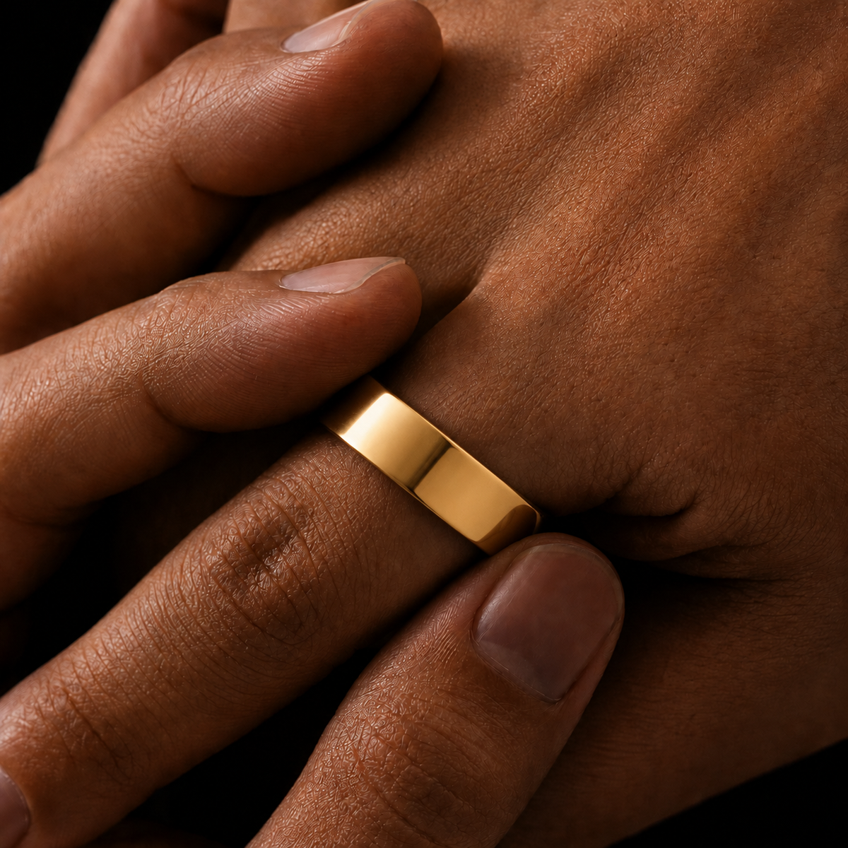 A close-up of a polished yellow gold band ring worn on a finger, shown against a person's skin with a dark background.
