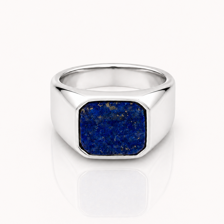 A silver signet ring featuring a square-cut blue lapis lazuli stone, displayed on a clean white reflective surface.