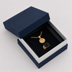 A gold coin pendant necklace and matching ring displayed inside an open navy blue jewelry box with a black velvet insert. The embossed brand name 'OUTRAGE London' is visible on the navy lid.