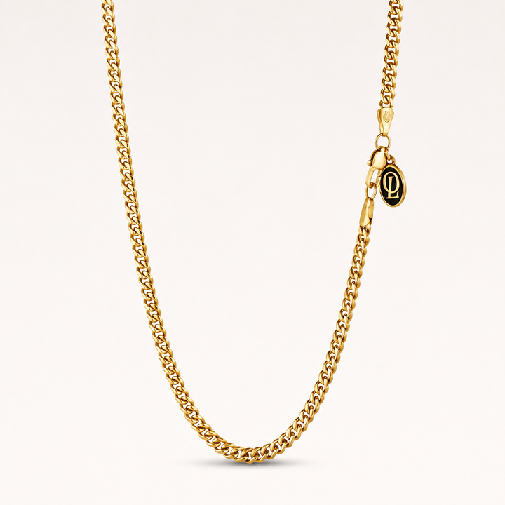 A gold-toned chain necklace with a lobster clasp and a small oval pendant featuring a black background and gold monogram, displayed on a clean off-white background.