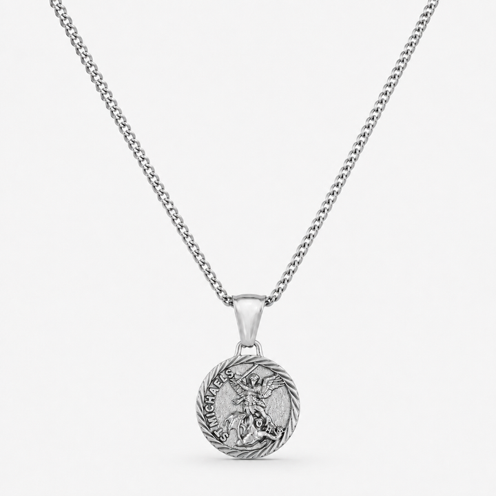 A silver-toned chain necklace with a round pendant featuring a detailed dragon design and the words 'HARD AS A BONE' on a light gray background.