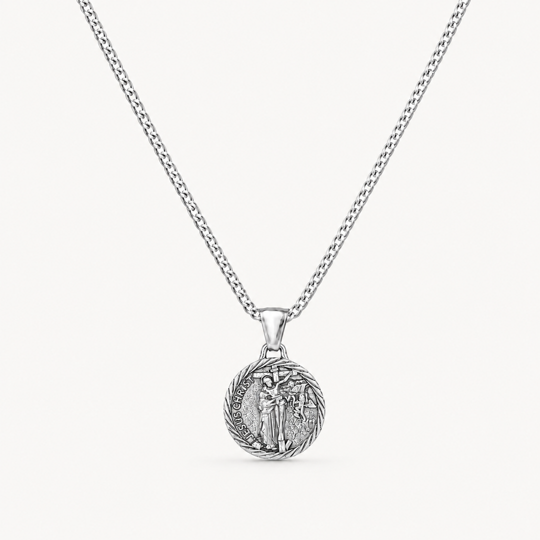 A silver chain necklace with a round, detailed pendant featuring a religious figure, shown against a light off-white background.
