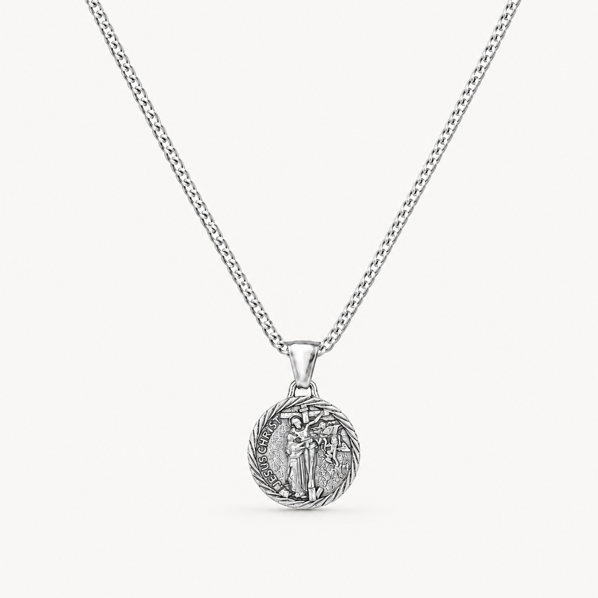A silver chain necklace with a round, detailed pendant featuring a religious figure, shown against a light off-white background.