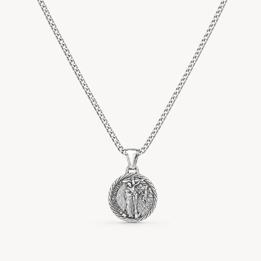 A silver chain necklace with a round, detailed pendant featuring a religious figure, shown against a light off-white background.