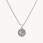 A silver chain necklace with a round, detailed pendant featuring a religious figure, shown against a light off-white background.