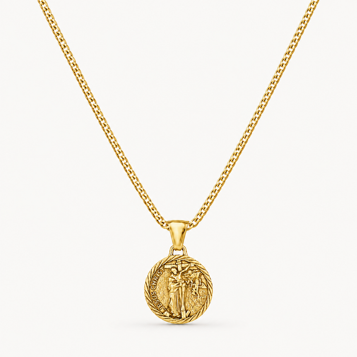 A gold chain necklace with a circular medallion pendant featuring an embossed figure, shown against a clean off-white background.