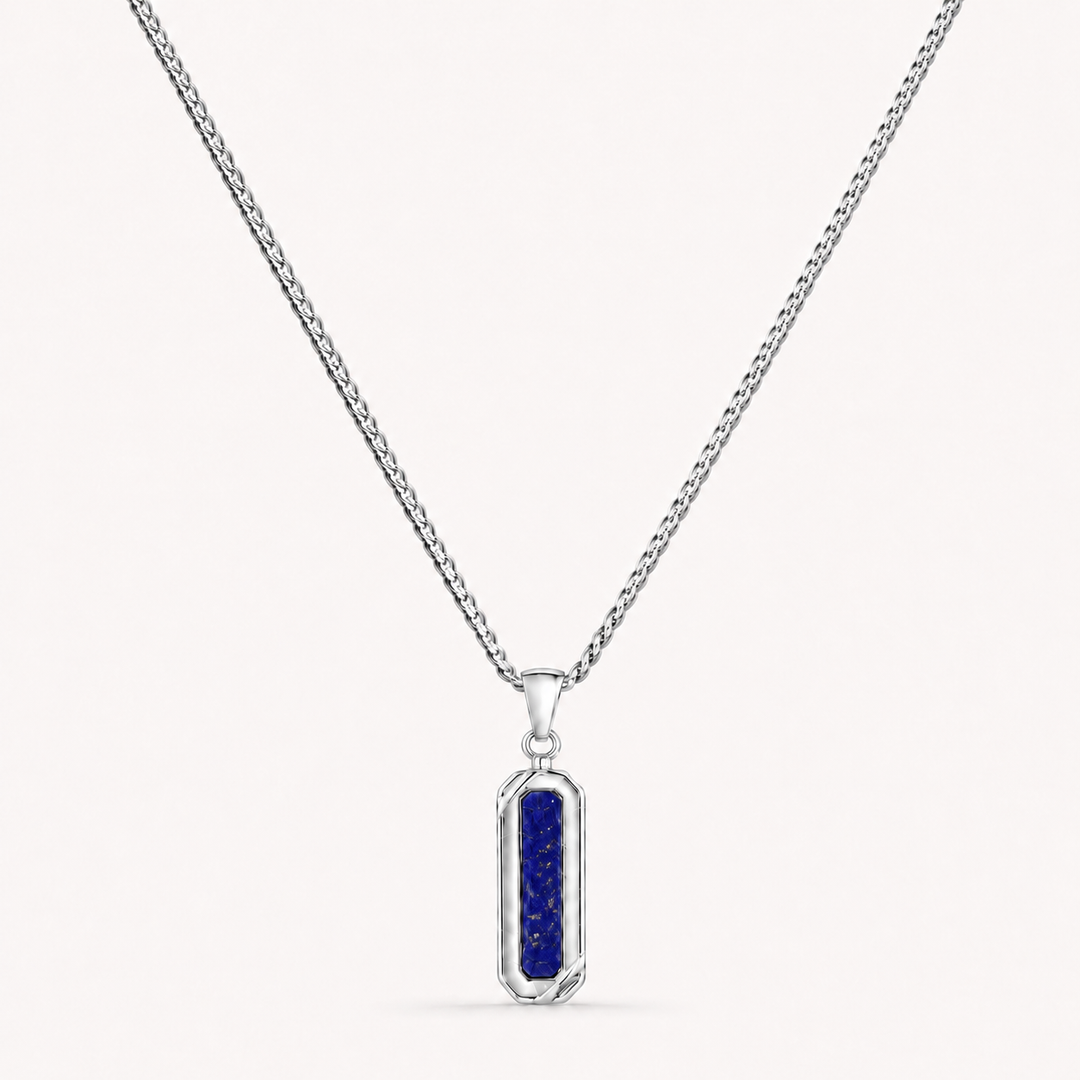 A silver-toned chain necklace with a vertical rectangular pendant featuring a deep blue textured center, shown on a light off-white background.