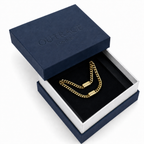A gold chain necklace with a clasp is displayed inside an open navy blue and white jewelry box. The embossed brand name 'OUTRAGE LONDON' is visible on the navy lid.