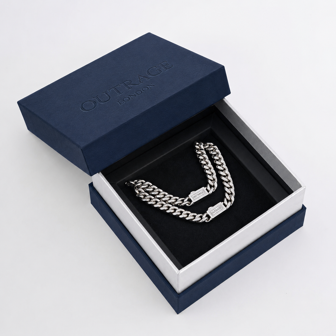 A silver-toned double-layered chain necklace with rectangular links, presented inside an open navy blue Outrage London jewelry box with a black velvet insert.