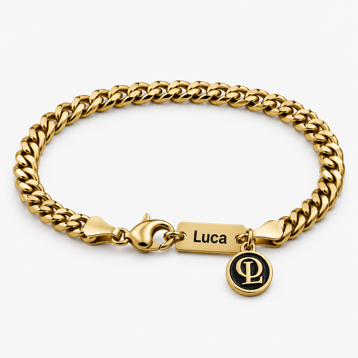 A gold-toned Cuban link bracelet with a lobster clasp, a rectangular nameplate engraved with the name 'Luca', and a small round black-and-gold charm featuring interlocking letters, shown on a light gray background.