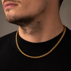 A close-up of a man's neck and lower face wearing a thick, shiny gold chain necklace over a black crewneck shirt.