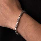 A close-up of a person's wrist wearing a thick, polished silver chain link bracelet against a black shirt background.