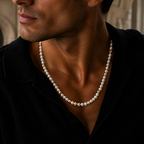 A close-up of a man wearing a pearl necklace with gold spacer beads, styled with a black shirt.