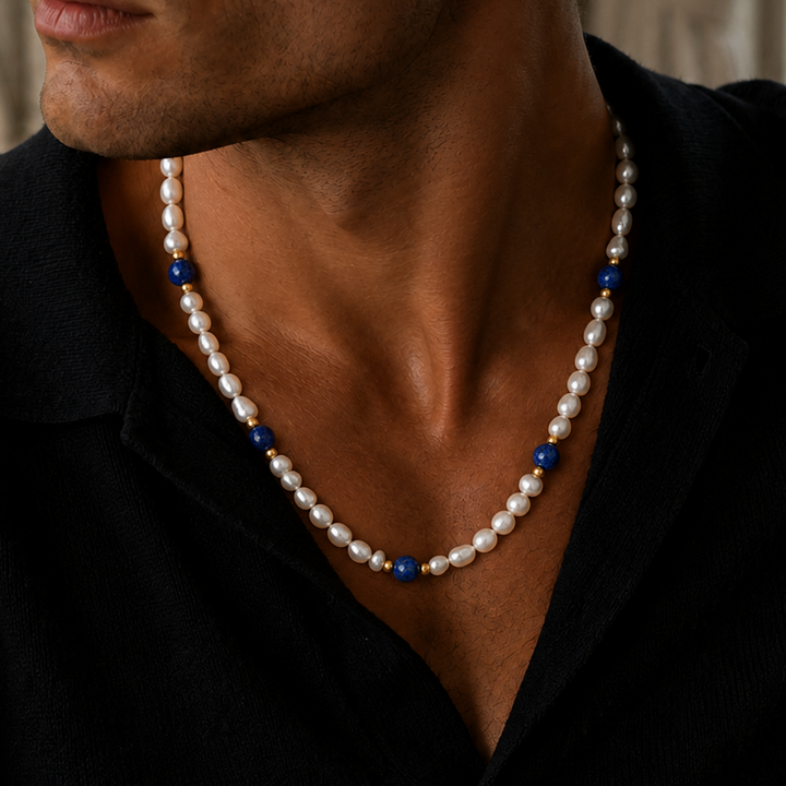 A close-up of a man wearing a beaded necklace with white pearl-like beads, small gold spacer beads, and blue accent beads, paired with a black shirt.
