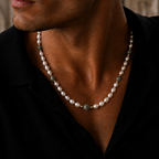 A close-up of a man wearing a pearl necklace with a central green stone accent, styled with a black shirt.
