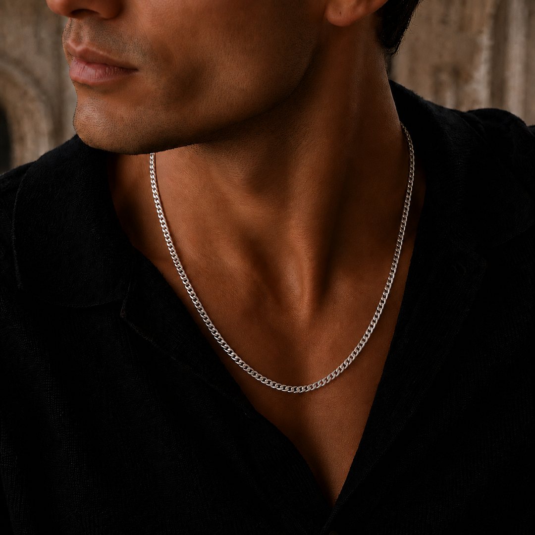 A close-up of a man wearing a silver chain necklace over a black shirt, highlighting the necklace against his neck.
