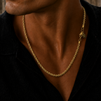A close-up of a man wearing a gold rope chain necklace with a star charm and logo tag, styled with a black shirt.