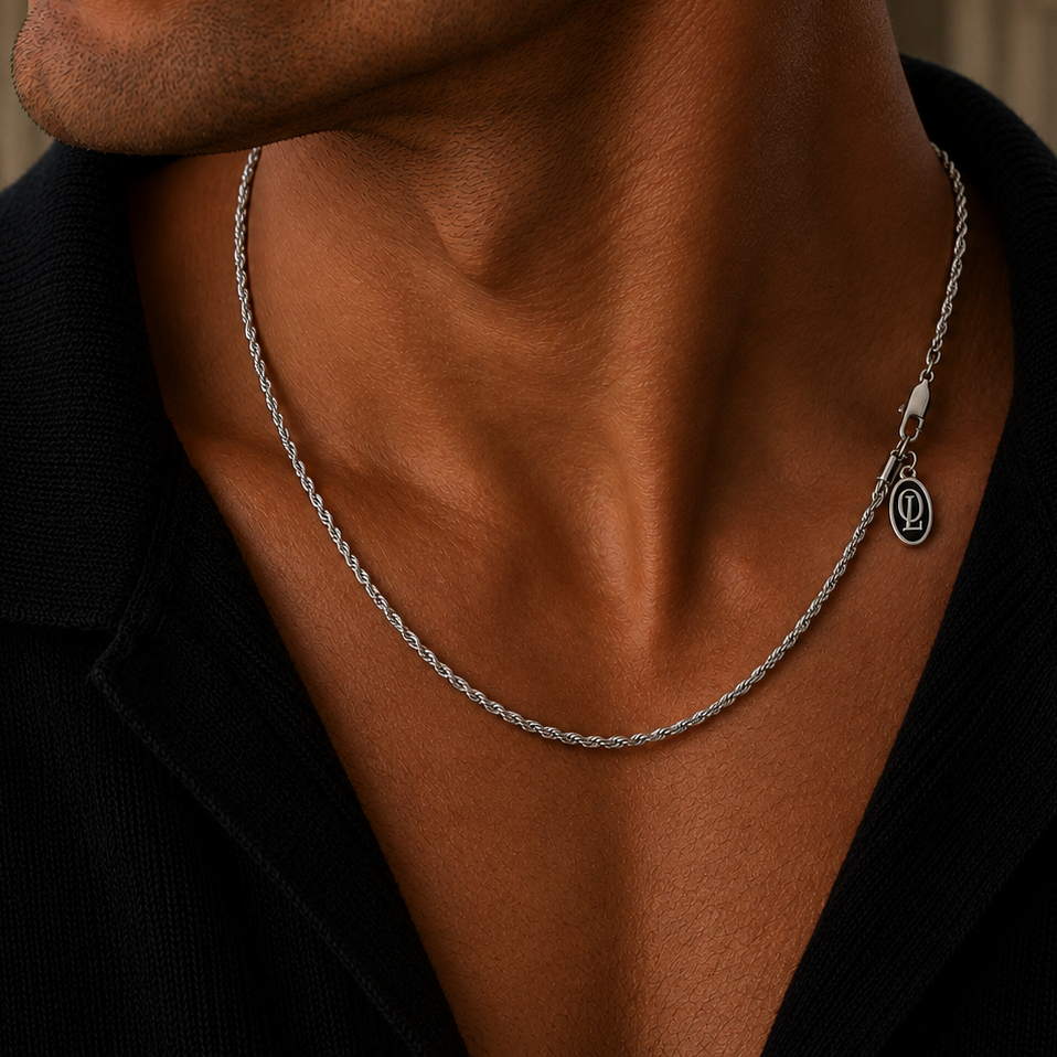 A close-up lifestyle shot of a man wearing a silver rope chain necklace with a small circular interlocking 'D' logo charm, styled with a black collared shirt.